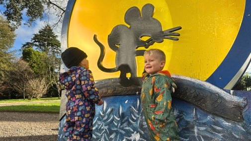 Two toddlers in rain suits smile and interact with the Gruffalo's Child trail at Saltram